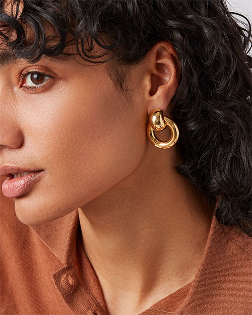A woman adorned with shiny gold hoop earrings, highlighting her fashionable and chic appearance.
