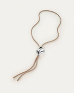 A bolo tie, showcasing a unique seashell shaped silver pendant on a tan cord necklace. The pendant has an abstract, flowing design and is positioned at the center of the chest.