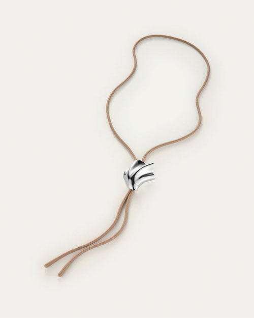 A bolo tie, showcasing a unique seashell shaped silver pendant on a tan cord necklace. The pendant has an abstract, flowing design and is positioned at the center of the chest.