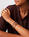 A model wearing a brown knit button-down top. She is wearing multiple gold bangles and a silver bracelet featuring small spherical beads evenly spaced around it.