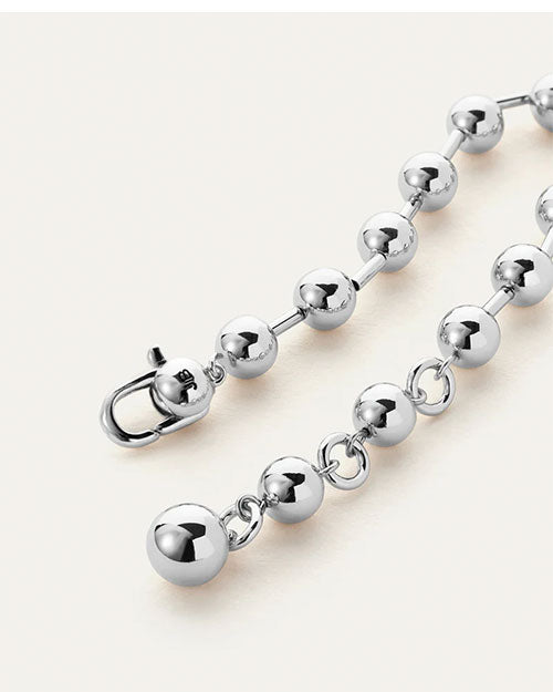 A close-up view of a silver bracelet with spherical beads and a clasp engraved with the letters "JB", resting against a white background.