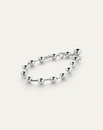 A silver bracelet with round beads evenly spaced around it, laid against a white background.