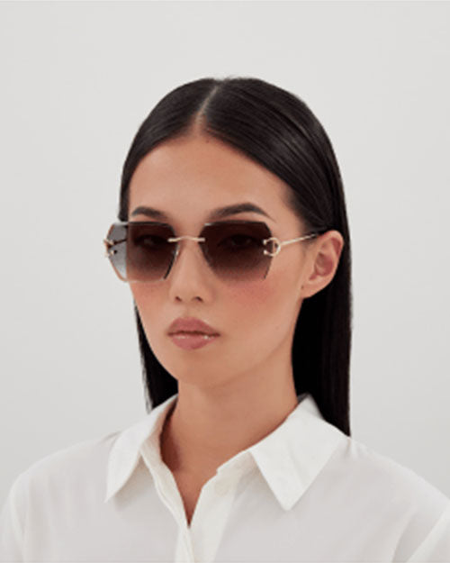 A headshot of a person wearing a white collared shirt and a pair of square sunglasses with thin gold-colored frames and dark lenses. The hinges form a C shape.