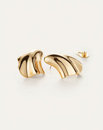 A pair of gold earrings laid against a white background with an abstract, fluid design which resembles a seashell. One of the ear backings is shown.