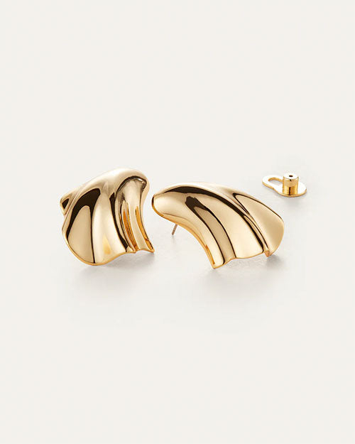 A pair of gold earrings laid against a white background with an abstract, fluid design which resembles a seashell. One of the ear backings is shown.