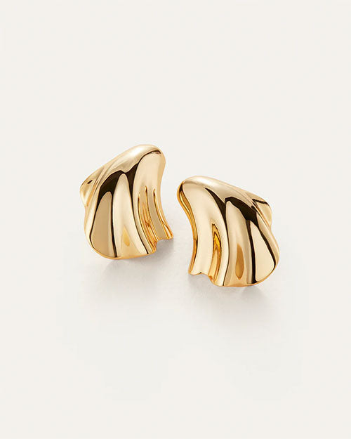 A pair of gold earrings laid against a white background with an abstract, fluid design resembling a seashell.
