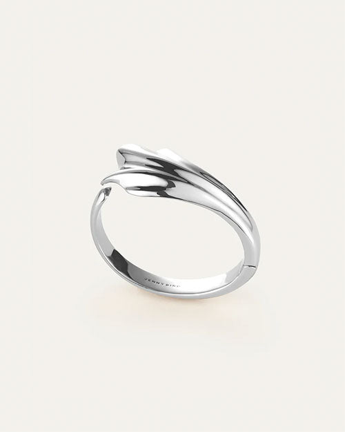 An overhead view of a gold cuff bracelet with an abstract, fluid design which resembles a seashell. The inside reads "JENNY BIRD".