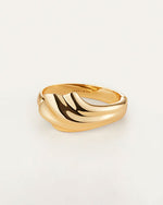 A gold cuff bracelet with an abstract, fluid design which resembles a seashell. The inside reads "JENNY BIRD"