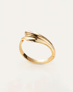 An overhead view of a gold cuff with an abstract, fluid design which resembles a seashell. The inside reads "JENNY BIRD"