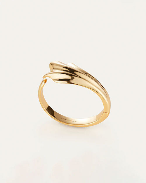 An overhead view of a gold cuff with an abstract, fluid design which resembles a seashell. The inside reads "JENNY BIRD"