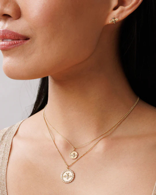 Close-up of a woman wearing gold necklaces and bee-shaped earrings against a neutral background