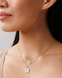 Close-up of a woman wearing gold necklaces and bee-shaped earrings against a neutral background