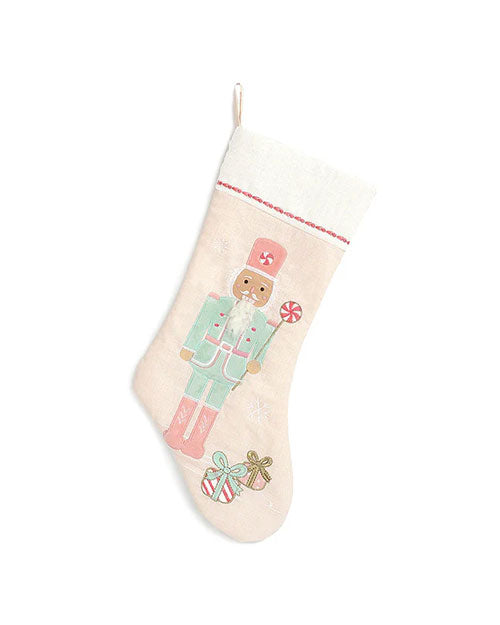 A Christmas stocking in front of a white background. The stocking features an embroidered design of a nutcracker soldier with two presents at its feet.