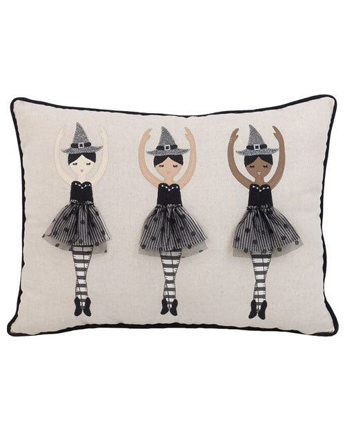 A rectangular pillow featuring three ballerina figures side by side dressed as witches, wearing black witch hats, black dresses with a tutus, and striped stockings standing in standing ballerina poses with their arms up above them. The pillow has black piping around the edges, and is placed against a white background.