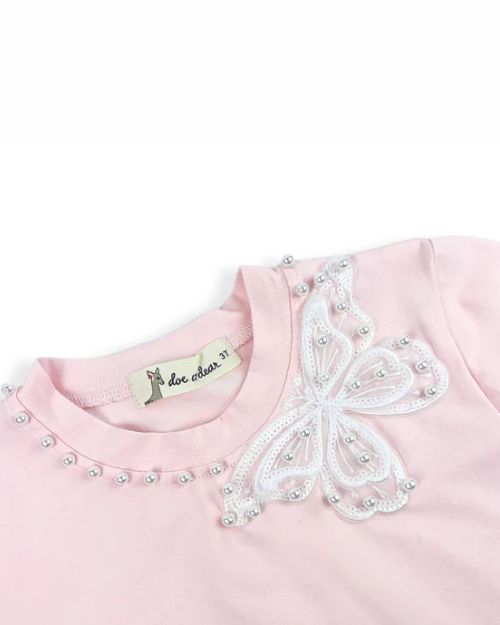 A pink tee with a white lace butterfly and pearl studs, combining a playful and sophisticated aesthetic.