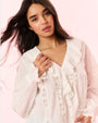 A waist-up view of a brunette model wearing a white blouse featuring a ruffled neckline and wrists, and vertical lace down the torso.