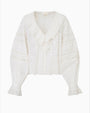 A white blouse in front of a white background featuring elegant, ruffled wrists and neckline, featuring vertical lace detailing on the torso and horizontal detailing on the arms.