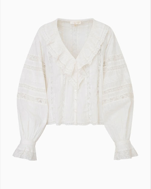 A white blouse in front of a white background featuring elegant, ruffled wrists and neckline, featuring vertical lace detailing on the torso and horizontal detailing on the arms.
