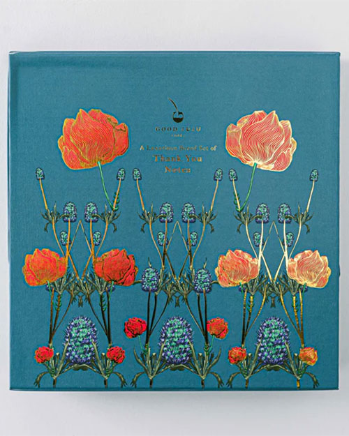 A blue-covered stationary box, "Good Juju Ink Enchanted Garden," embellished with floral designs.