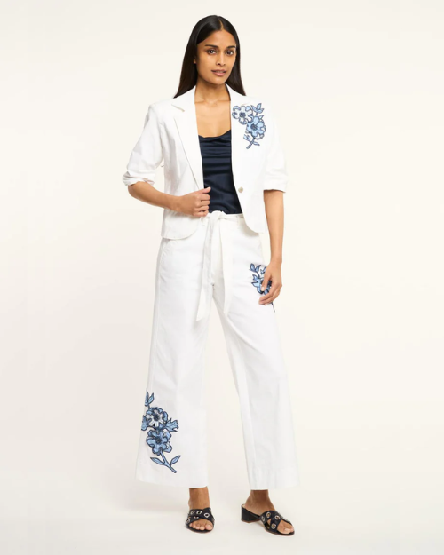 Woman wearing a white outfit with blue floral embroidery on a white background