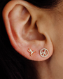 Close-up of an ear wearing two earrings: humming bird and a peace symbol design.