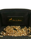 Interior view of a black quilted vanity-style handbag showing a gold chain strap and a black fabric label with a gold deer logo and the text ‘doe a dear.