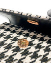 Close-up of the inside flap of a black and white houndstooth handbag, showing a magnetic snap closure with metallic circular fasteners.