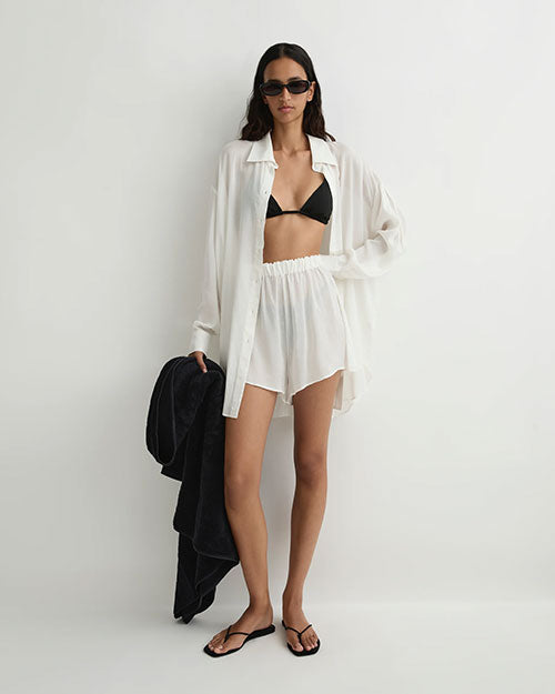 Person wearing a sheer white shirt and matching sheer white shorts. They paired it with a black bikini and black flip flops.