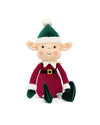 Plush elf toy wearing a green hat with a white pom-pom, red outfit with white cuffs and collar, black belt with yellow buckle, green shoes, and striped socks, featuring large ears, rosy cheeks, and a smiling face.
