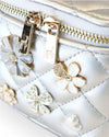 Close-up of a metallic silver quilted vanity-style handbag showing gold-tone zipper pulls and decorative floral embellishments in white, silver, and crystal accents.