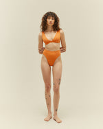 A full view of a model wearing a matching two-piece orange swim suit. The top features a low plunge V neckline. 