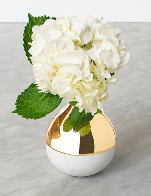 Marble bud vase with flowers on top of a table.