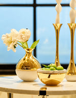Marble bud vase with flowers on top of a table with 2 candle holders and a bowl. 