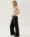 A side-view of a high-waisted, straight-leg black silk pant. The pants have a smooth texture and a relaxed fit. The model is styled with a white tank.