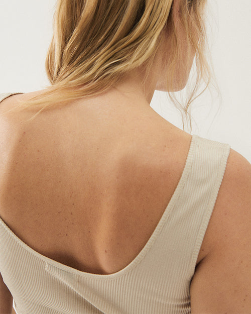A close-up overhead view of a blonde models' back wearing a white, open round backed shirt with a ribbed material. The background is plain white.