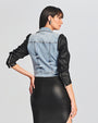 Back view of denim and leather jacket model with contrasting two-tone effect, featuring silver hardware, styled with a form-fitting black dress and metallic clutch.