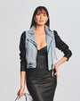  Denim and leather jacket model with contrasting two-tone effect, featuring silver hardware, styled with a form-fitting black dress and metallic clutch.