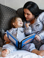 Mom and kid on the bed, mom reading a kids book while wearing Post Oak Pajamas.