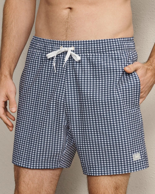 Navy and white gingham swim trunks featuring a classic check pattern, elastic waistband, white drawstring closure, and side pockets.