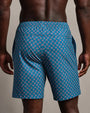 Back view of blue geometric print swim trunks featuring a red and white diamond pattern, elastic waistband, and relaxed fit.