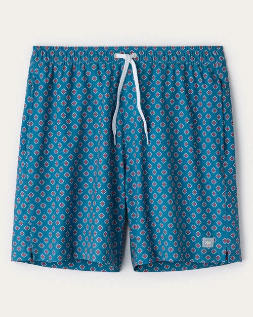 Blue geometric print swim trunks with a red and white diamond pattern, elastic waistband, white drawstring closure, and relaxed fit displayed on a light gray background.