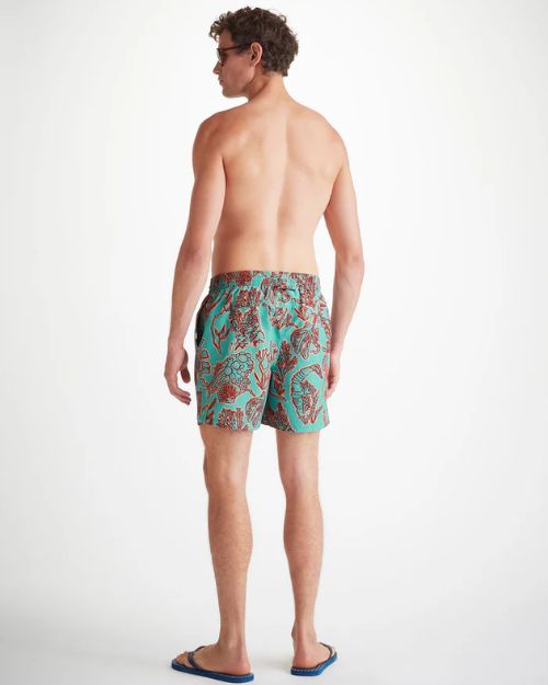 An image of a man standing backwards wearing sunglasses and swim shorts. 
 The turquoise men's swim shorts has dark red shadowed with neon orange drawings of an array of seaweed, kelp, and octopuses' legs.  The top of the swim shorts has an elastic waistband with a drawstring tie.