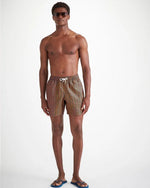 A mad standing with sunglasses on wearing men's swim shorts that are blue and have orange nautical knots and ropes going vertically down in rows across the swim shorts.  The swim shorts have a fully elasticated waistband and white drawstring tie.  He has blue flip flops on his feet.