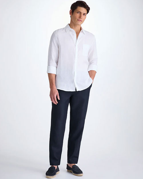 A man wearing a white shirt and navy pants stands confidently, showcasing a professional appearance.