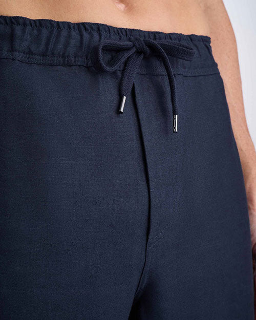 A close-up of a man wearing navy pants, showcasing the fabric and fit against a neutral background.
