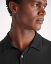 An image of a man from his shoulders to the top of his hair line showing off the black color short sleeve polo shirt with a ribbed collar and mother of pearl buttons