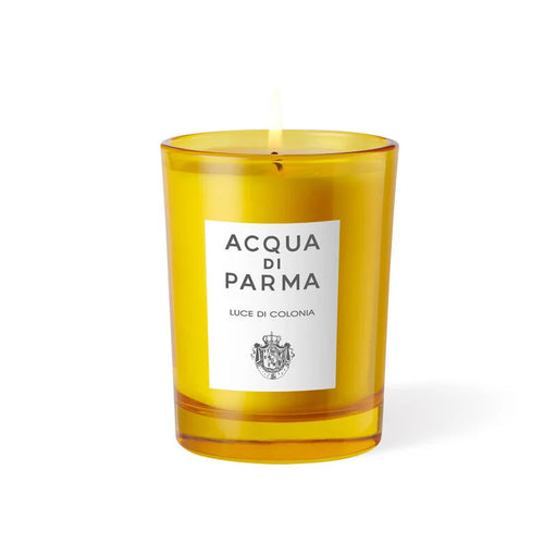 A lit Acqua Parma orange candle in a decorative glass, casting a soft light in a serene setting.