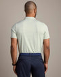 Back view of a light green striped performance polo shirt with short sleeves, subtle horizontal stripes, and an athletic fit, paired with navy pants.