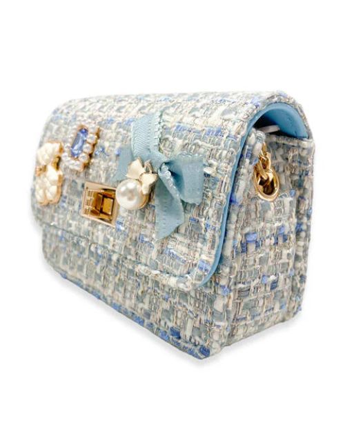 Side view of the little girls blue tweed purse showing the blue bow charm with the pearl dangling from the front and the gold chain tucked inside the purse to show that you can use it as a clutch purse as well