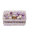 Purple tweed little girls purse with a quilted purple and gold bear charm, purple jewel with little pearls around charm, gold twist clasp, and a small purple bow with a pearl dangling off the middle of the bow on the front flap of the purse. 